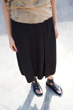 Crafted black midi skirt, highlighting pleated design and raw hem detail.