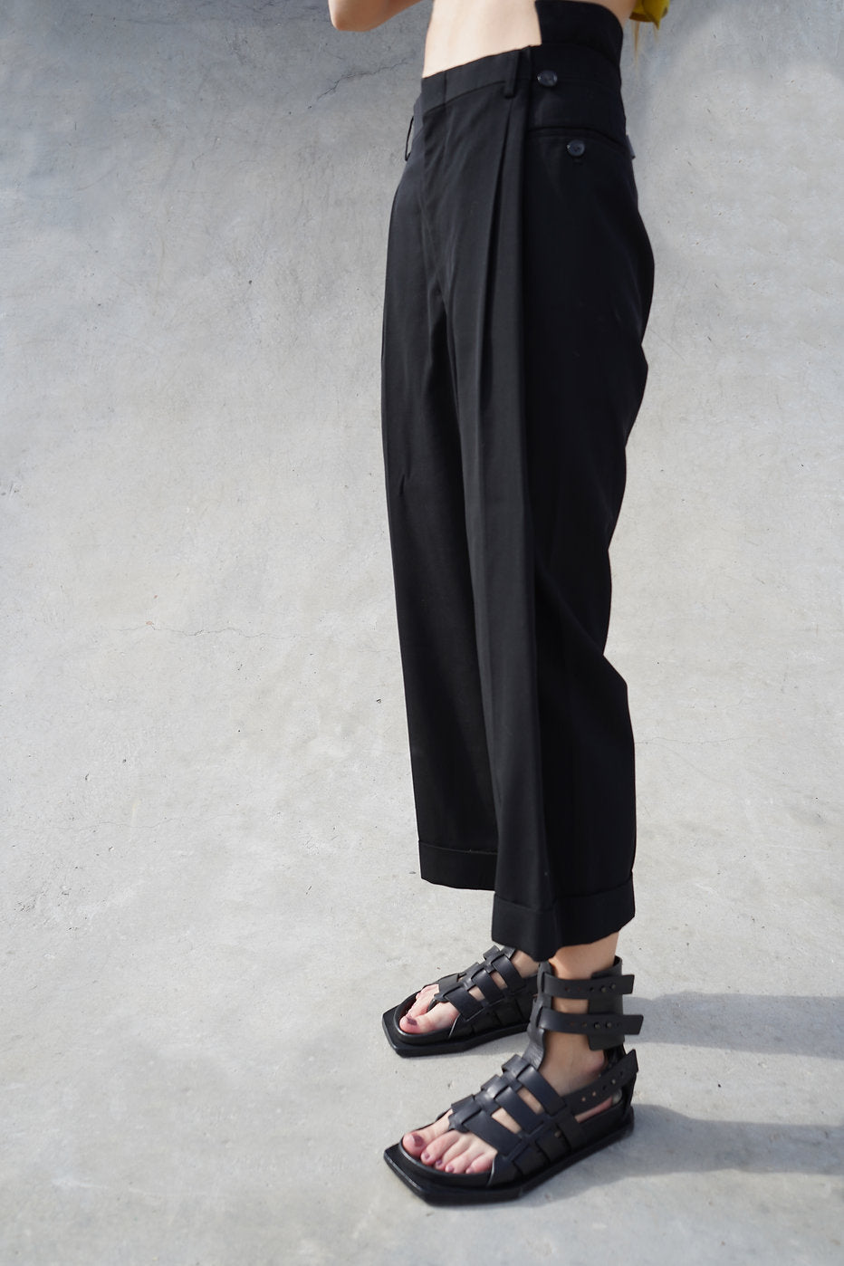 Side view of black pleated tapered pants, highlighting the chic cropped length